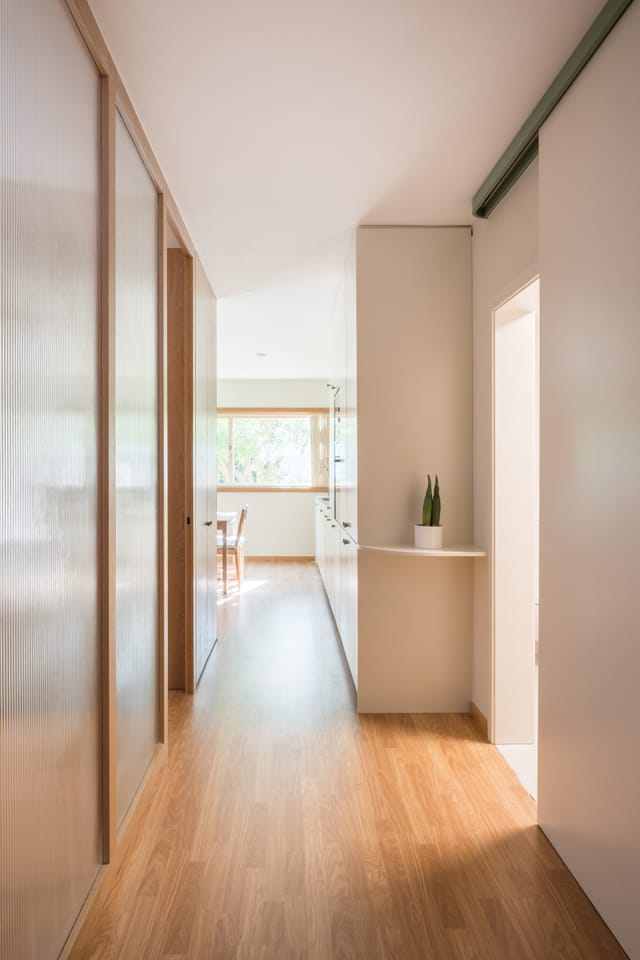 Long corridor lined with reeded-glass sliding panels and white storage, opening onto the daylit living space.
