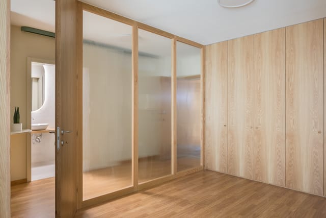 Oak-framed reeded-glass partition and full-height oak wardrobes, with the bathroom visible through an open door.