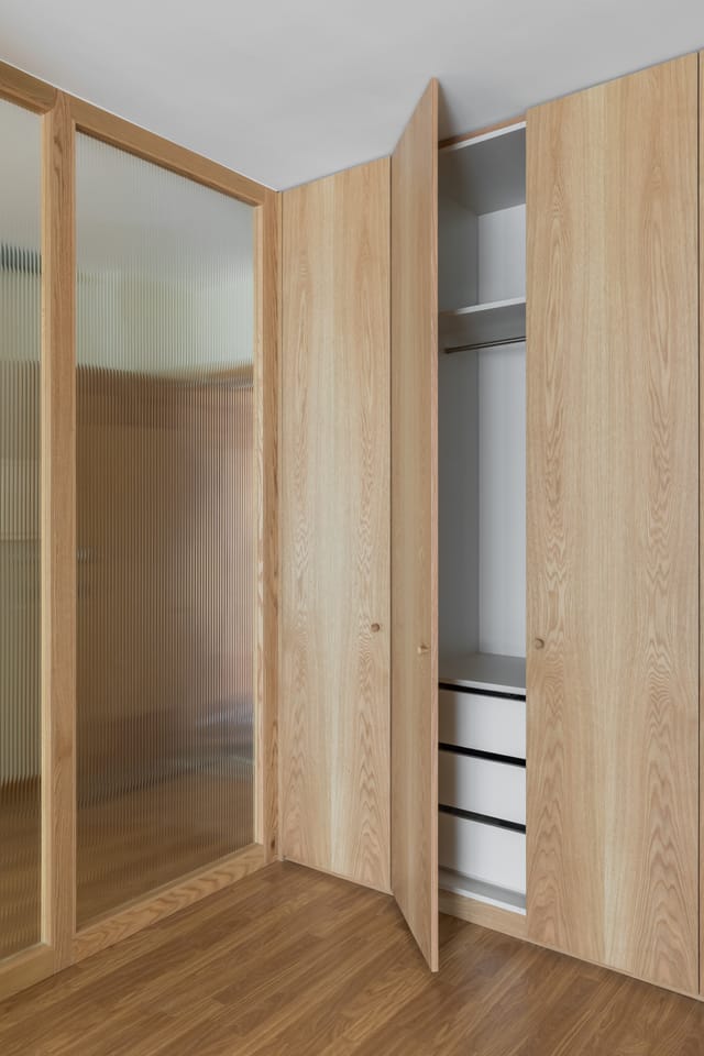 Full-height oak wardrobe with one door open, showing hanging space and drawers beside the glass partition.