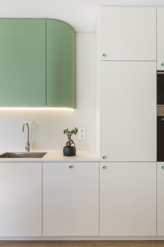 Detail of the rounded green wall cabinet with concealed lighting above the white kitchen worktop.