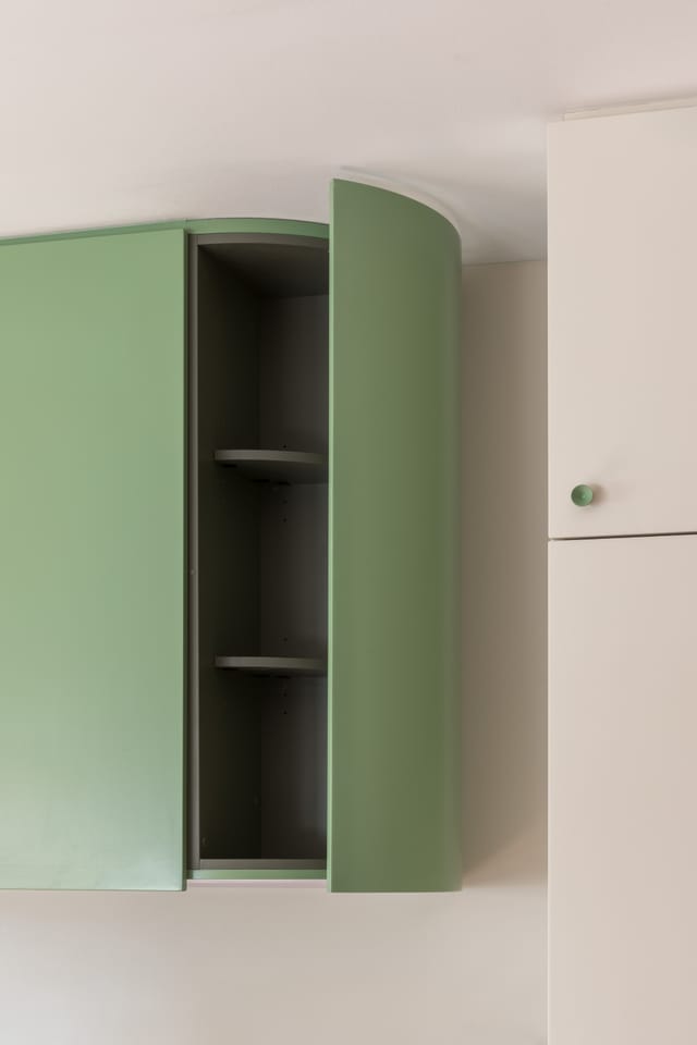 Detail of the curved green corner cabinet door opening to reveal shelves.