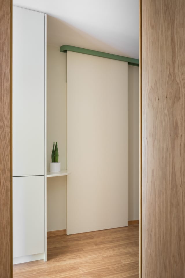 View between oak panels to a white sliding door on a green overhead track and a small curved shelf.