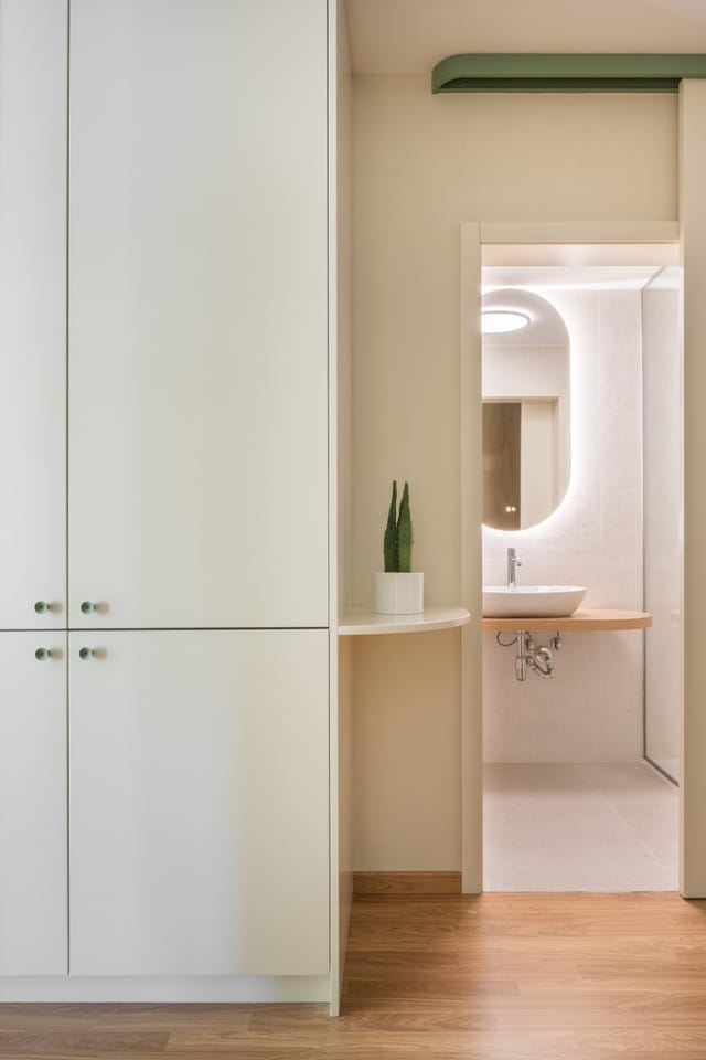 Tall white storage beside the bathroom door, showing a lit oval mirror and a round washbasin.