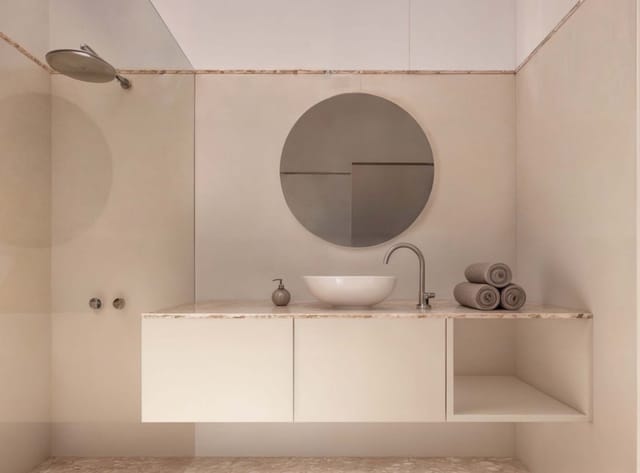 Rendering of the bathroom with floating vanity, round mirror and rain shower in warm neutral tones.