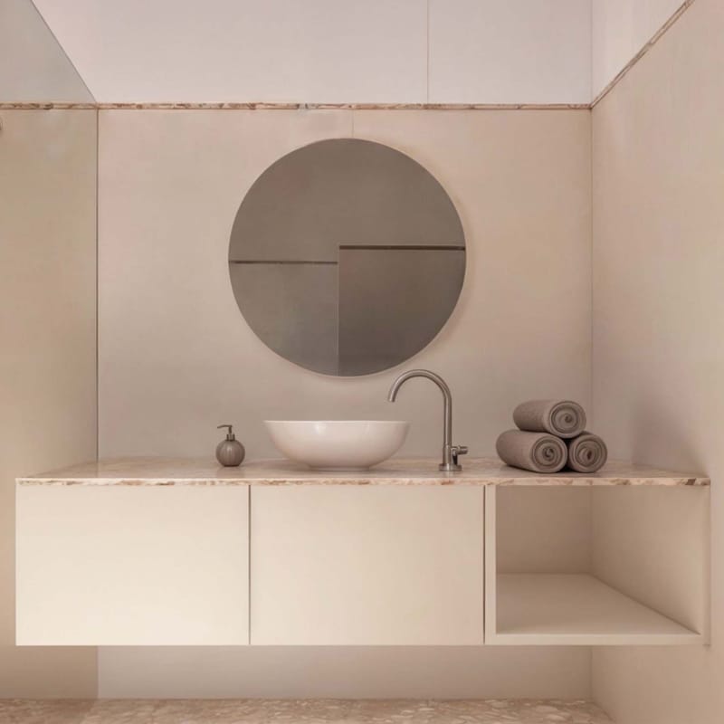 Rendering of a bathroom with a floating cream vanity, round vessel sink and round mirror on pink plaster.