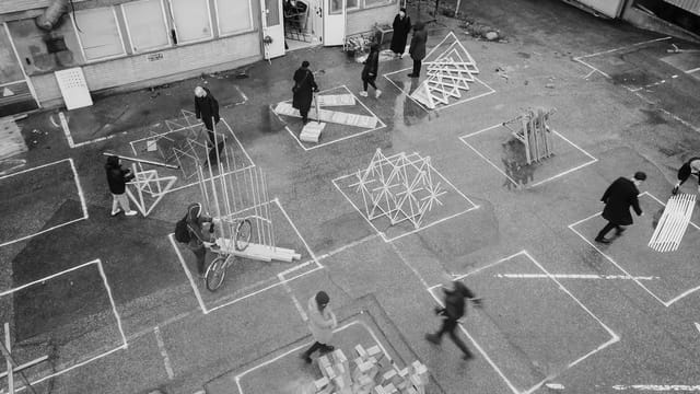 Black-and-white view from above of students assembling 1:1 timber prototypes in a courtyard.