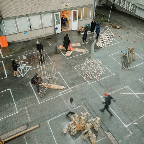 View from above of students building timber prototypes in a courtyard marked with chalk squares.